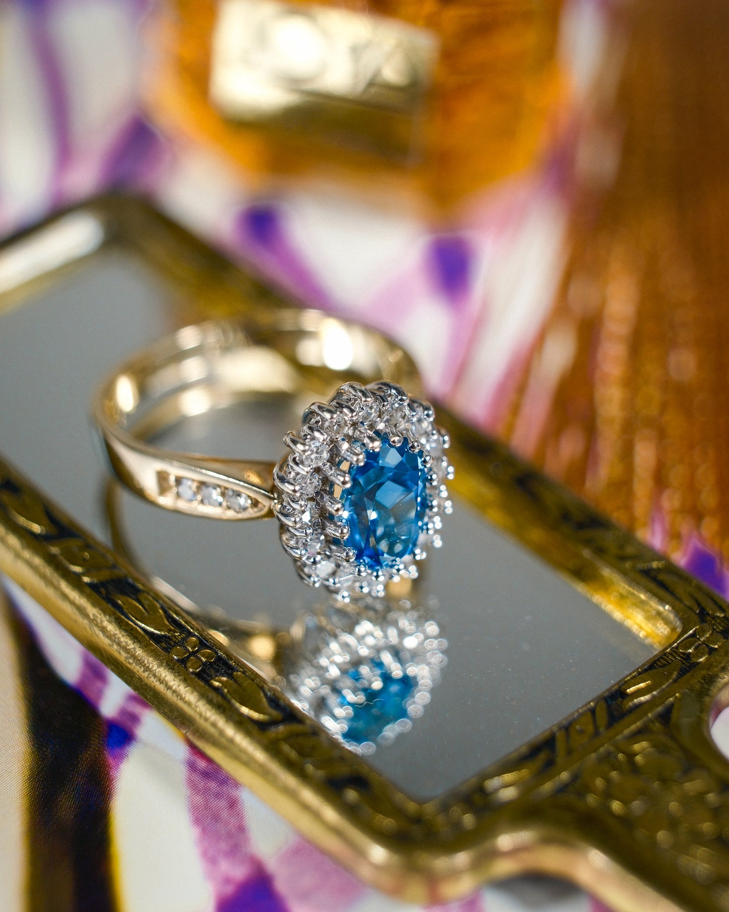 Een vintage ring liggend op een kleine spiegel met een blauwe topaas en diamanten van 9k geelgoud, product foto van de lijn Milena van The Vintage Company