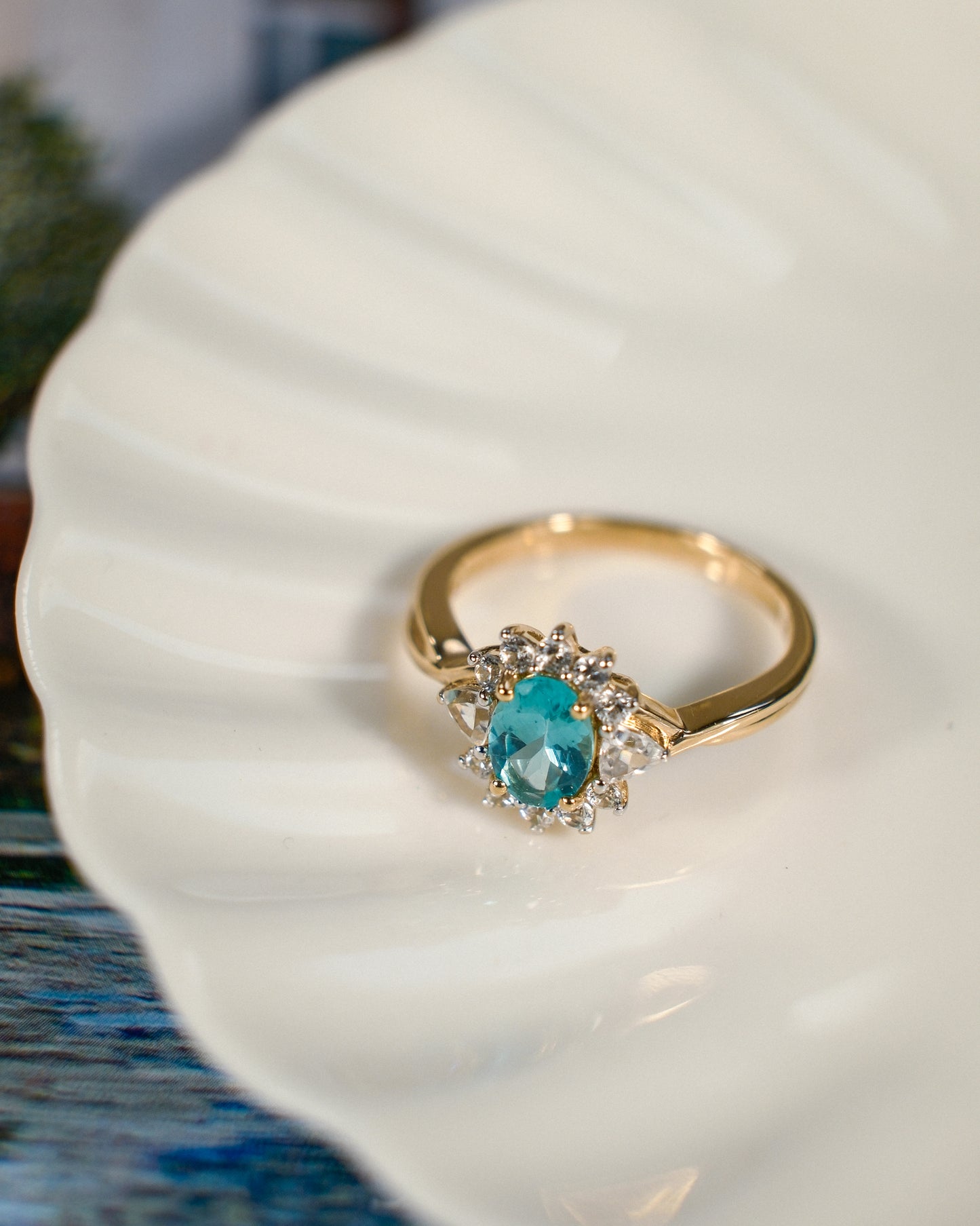 Een vintage ring op een wit schaaltje met een blauw/groenige kwarts edelsteen en zirkonia van 9k geelgoud, product foto van de lijn Armelia van The Vintage Company