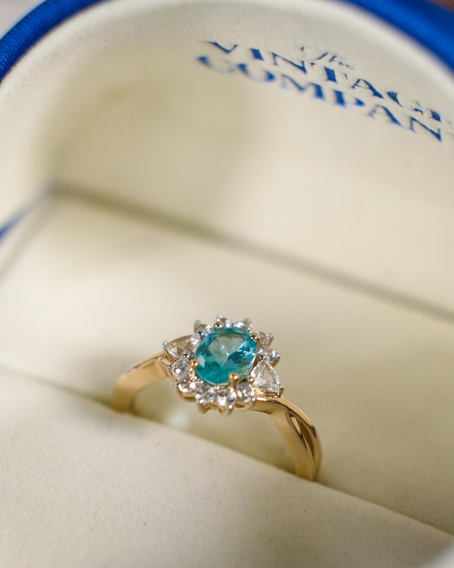 Een vintage ring in een blauw sieradendoosje van The Vintage Company met een blauw/groenige kwarts edelsteen en zirkonia van 9k geelgoud, product foto van de lijn Armelia van The Vintage Company