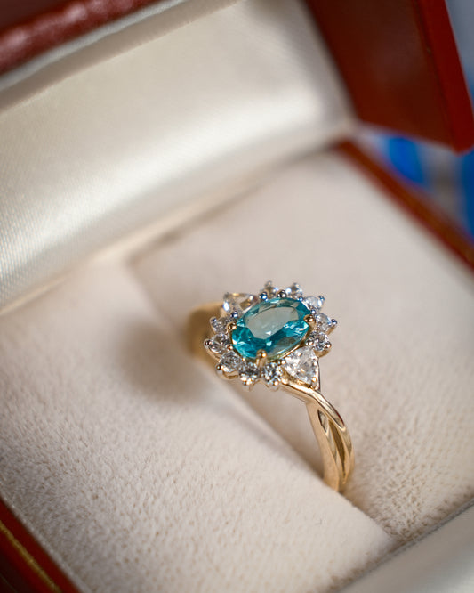 Een vintage ring in een rood sieradendoosje met een blauw/groenige kwarts edelsteen en zirkonia van 9k geelgoud, product foto van de lijn Armelia van The Vintage Company